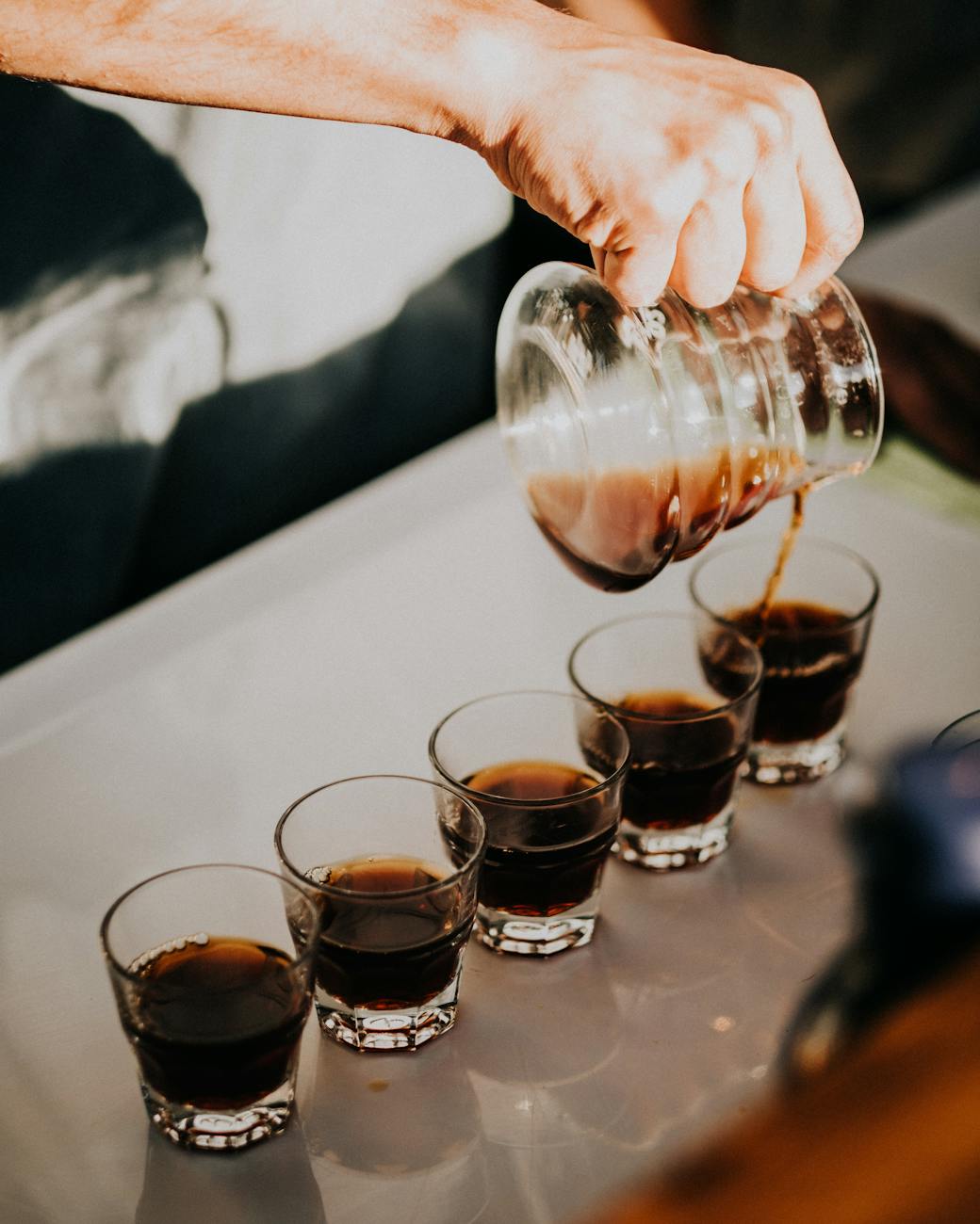 a person pouring black coffee on clear glasses